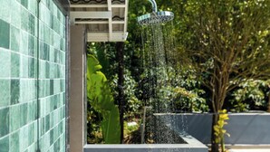 A showerhead with water flowing into a rectangular basin, set against a tiled wall and surrounded by greenery. - KAVA RETREAT (Chikkamagaluru)