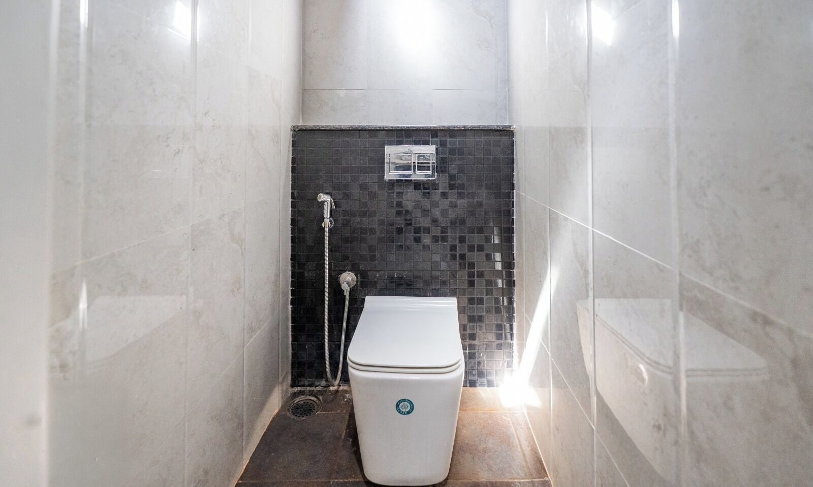 A small, modern bathroom with a white toilet, a shower with a handheld showerhead, and a tiled wall.