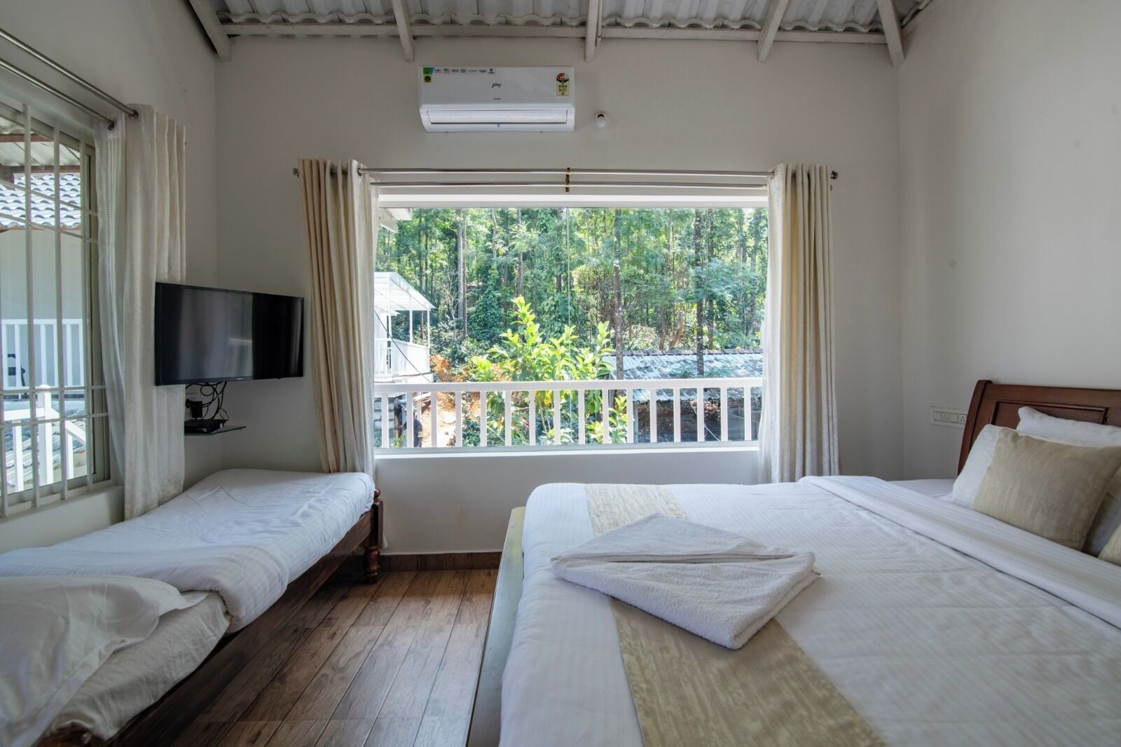 A room with two beds, a TV, and a balcony with a view of trees.