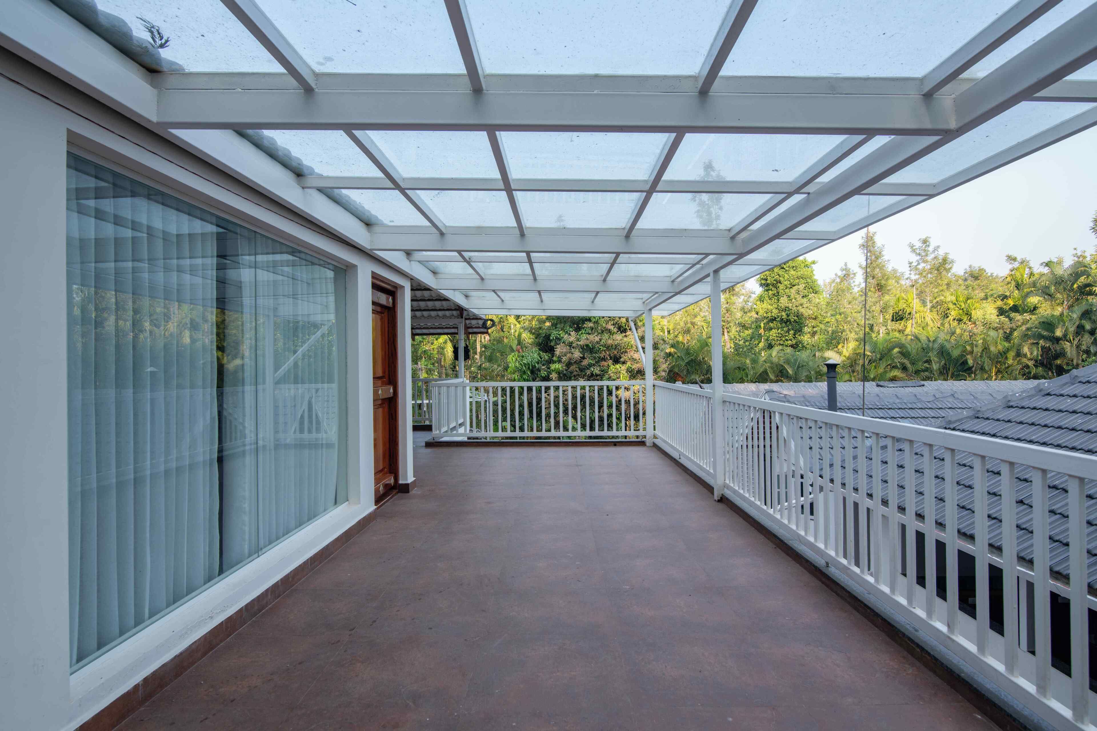 A covered balcony with a glass enclosure, white railings, and a view of greenery.