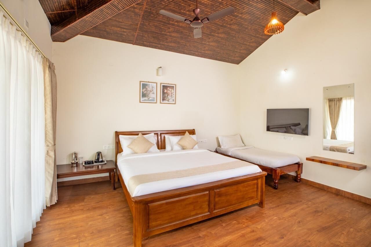 A room with a large bed, a smaller bed, a TV, a ceiling fan, and a wooden floor.