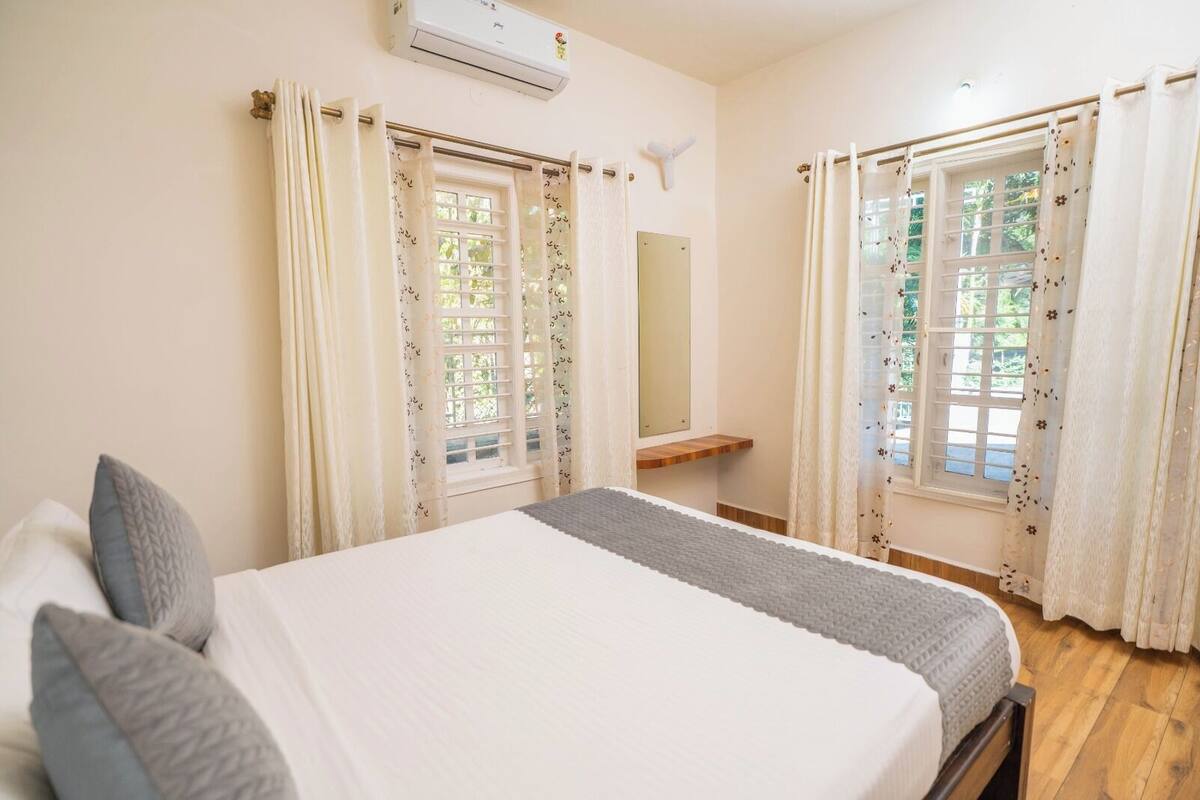 A bedroom with a bed, curtains, a mirror, and a window with a view.
