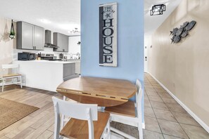A modern kitchen with grey cabinets, a central island, and a dining area with a wooden table and white chairs. - ☀️Walk to Beach | 4 Pools | Horizon South 59-104☀️ (Panama City Beach)
