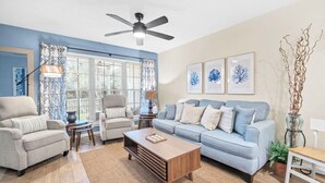 A living room with a sofa, armchairs, a coffee table, a ceiling fan, and artwork on the wall. - ☀️Walk to Beach | 4 Pools | Horizon South 59-104☀️ (Panama City Beach)