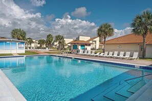 Une piscine d’un bleu éclatant, avec des chaises longues et des palmiers.