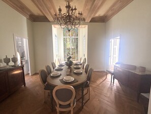 A dining room with a large wooden table set for six, surrounded by chairs, with a chandelier above. - Villa ADELAIDA (Nice)