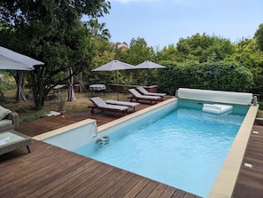 A swimming pool with lounge chairs and umbrellas, surrounded by greenery. - Villa ADELAIDA (Nice)