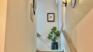 Un escalier en bois avec une rampe, un pot de fleurs et des œuvres d’art encadrées accrochées aux murs.
