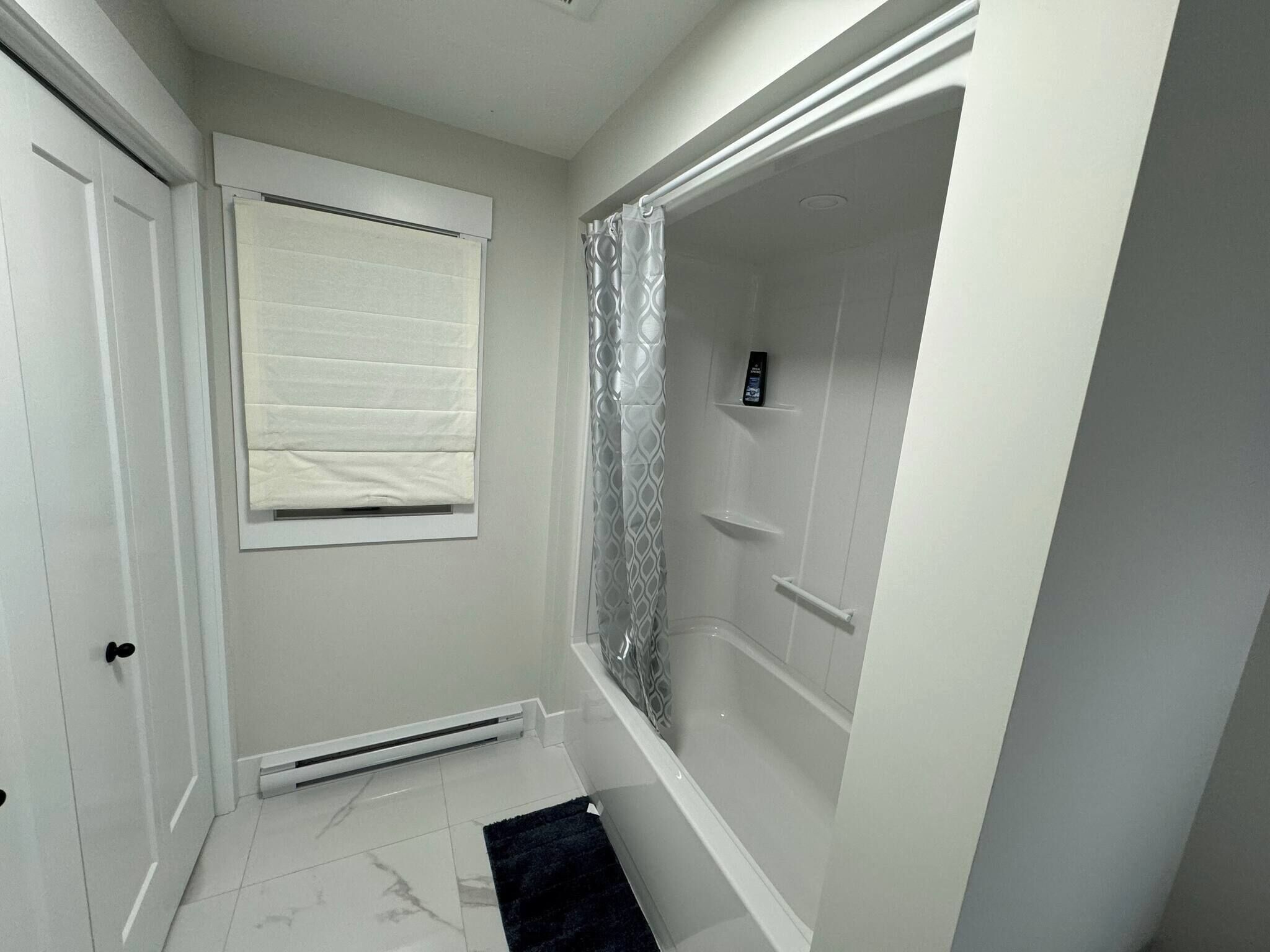 A bathroom with a shower, a toilet, a bidet, and a window with blinds.