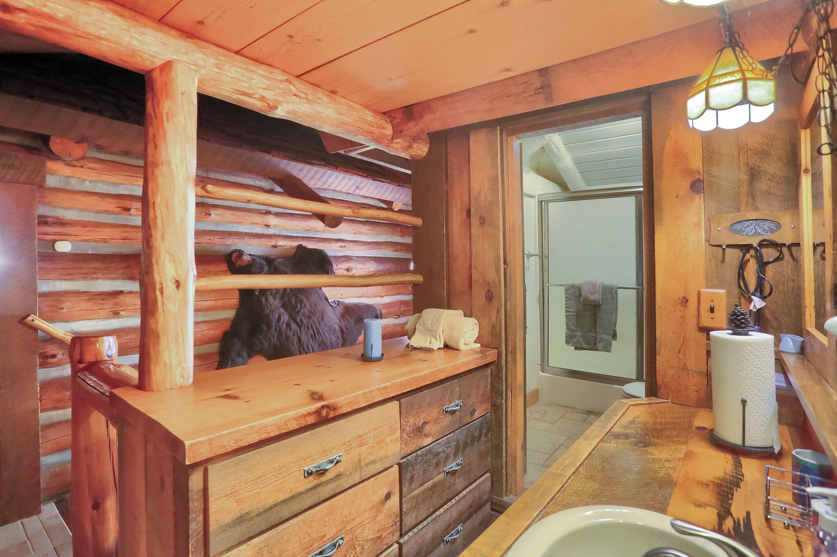 Interior de una cabaña de madera con tocador de madera, lámpara colgante y adorno de cabeza de oso.