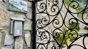 Mur de pedra amb una placa que diu 'Casa Malisa', una reixa de metall amb motius decoratius i una planta en test.