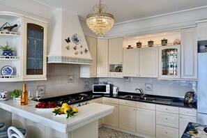 A kitchen with white cabinets, a central island, a chandelier, and decorative tiles. - Casa Malisa - Terrace sea view (Positano)