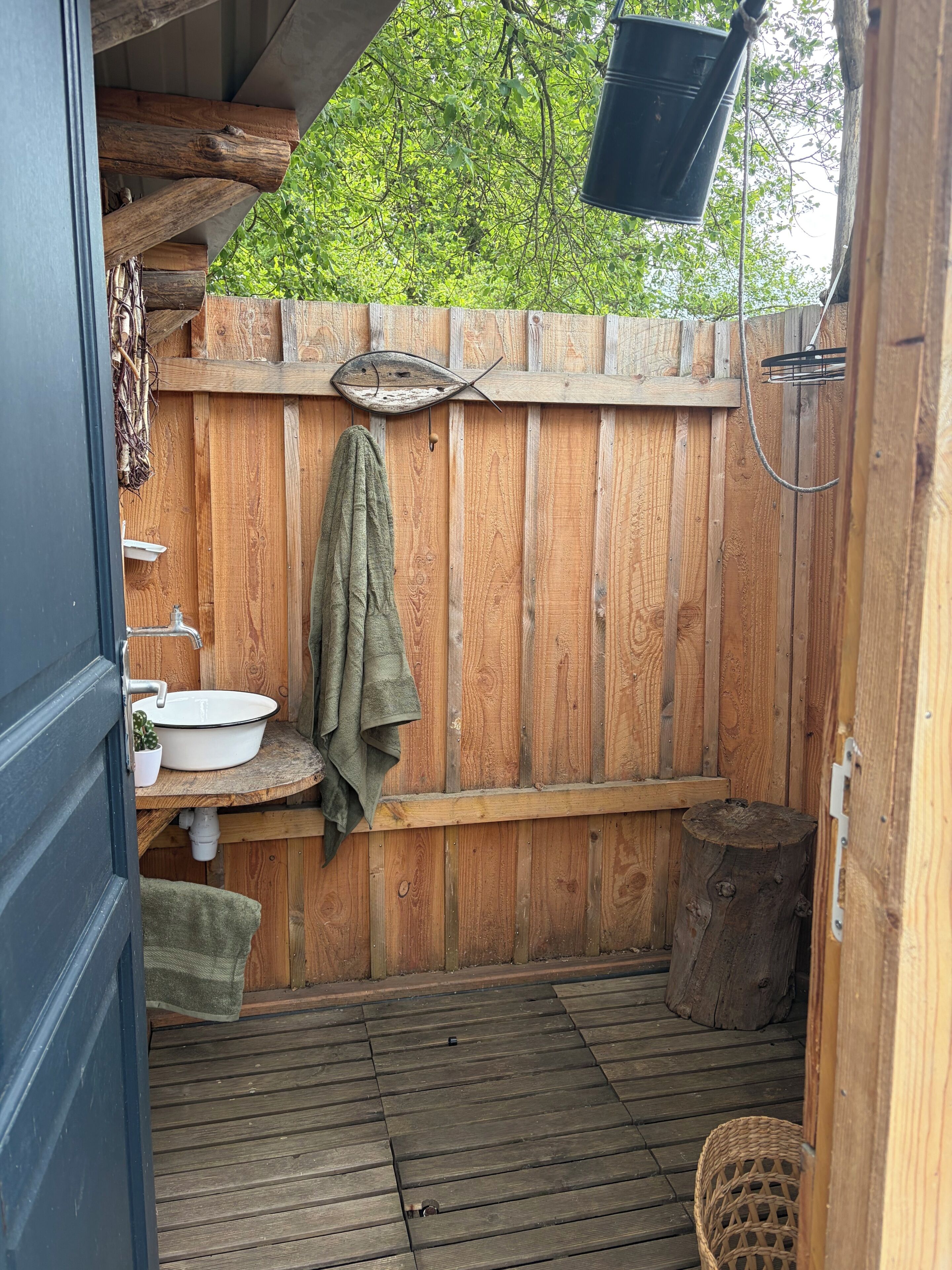 Una terraza de madera con un banco de madera, un lavamanos blanco y una toalla colgando.