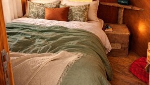 Un dormitorio acogedor con cabecera de madera, cama con ropa de cama verde y blanca, mesita de noche con lámpara y luces colgantes en el techo.