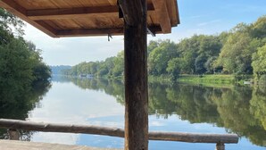 Una terraza de madera con un cuenco de vidrio y palillos, con vista a un río tranquilo bordeado de árboles.