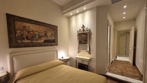 Ein Hotelzimmer mit Bett, einem Gemälde, einem Spiegel, einem Waschbecken und einem Flur, der in ein weiteres Zimmer führt.