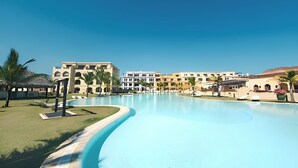 Een resort met een groot zwembad, meerdere gebouwen met balkons en palmbomen.