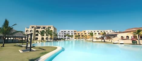 A resort with a large swimming pool, multiple buildings with balconies, and palm trees.