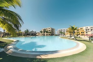 Una gran piscina de borde curvo, rodeada de césped cuidado y palmeras.
