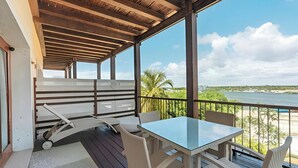 Een overdekt terras met een tafel en stoelen, met uitzicht op een strand en de oceaan.