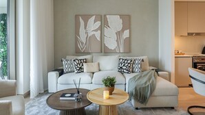 A modern living room with a sofa, two round coffee tables, and a potted plant. - 2BR  Apt in Dubai Creek Grove 3 (Dubai)