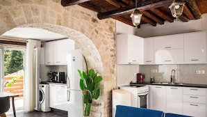 A kitchen with stone walls, white cabinets, a washing machine, and a dining area with a table and chairs. - Art House with Seaview by Konnect, Spartylas (Corfu)