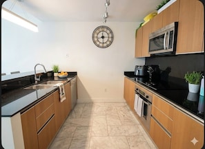 A modern kitchen with wooden cabinets, a black countertop, a stainless steel microwave, and a clock on the wall. - Brickell Luxury Miami High rise, King suite, 2BD 2BA, Parking free (Miami)