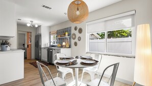 Una cucina moderna con mobili bianchi, un'area pranzo con un tavolo e sedie rotonde, e un'ampia finestra vista sull'esterno.