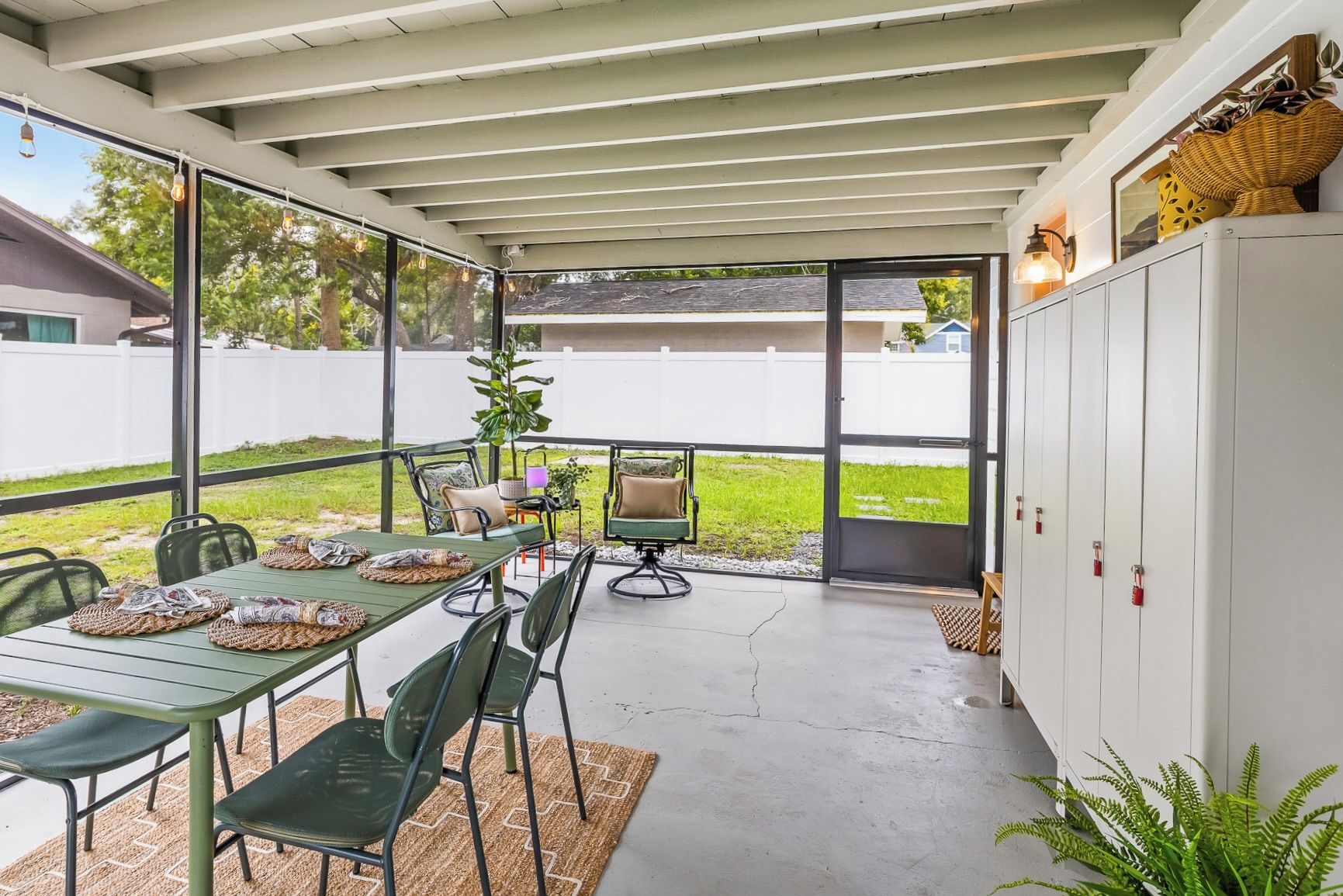 A covered patio area with a dining table set for four, surrounded by chairs, and a cabinet to the right.