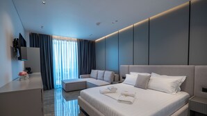 A modern hotel room with a large bed, a sofa, a desk, and a TV mounted on the wall. - Vila Era Beach 2 (Sarande)