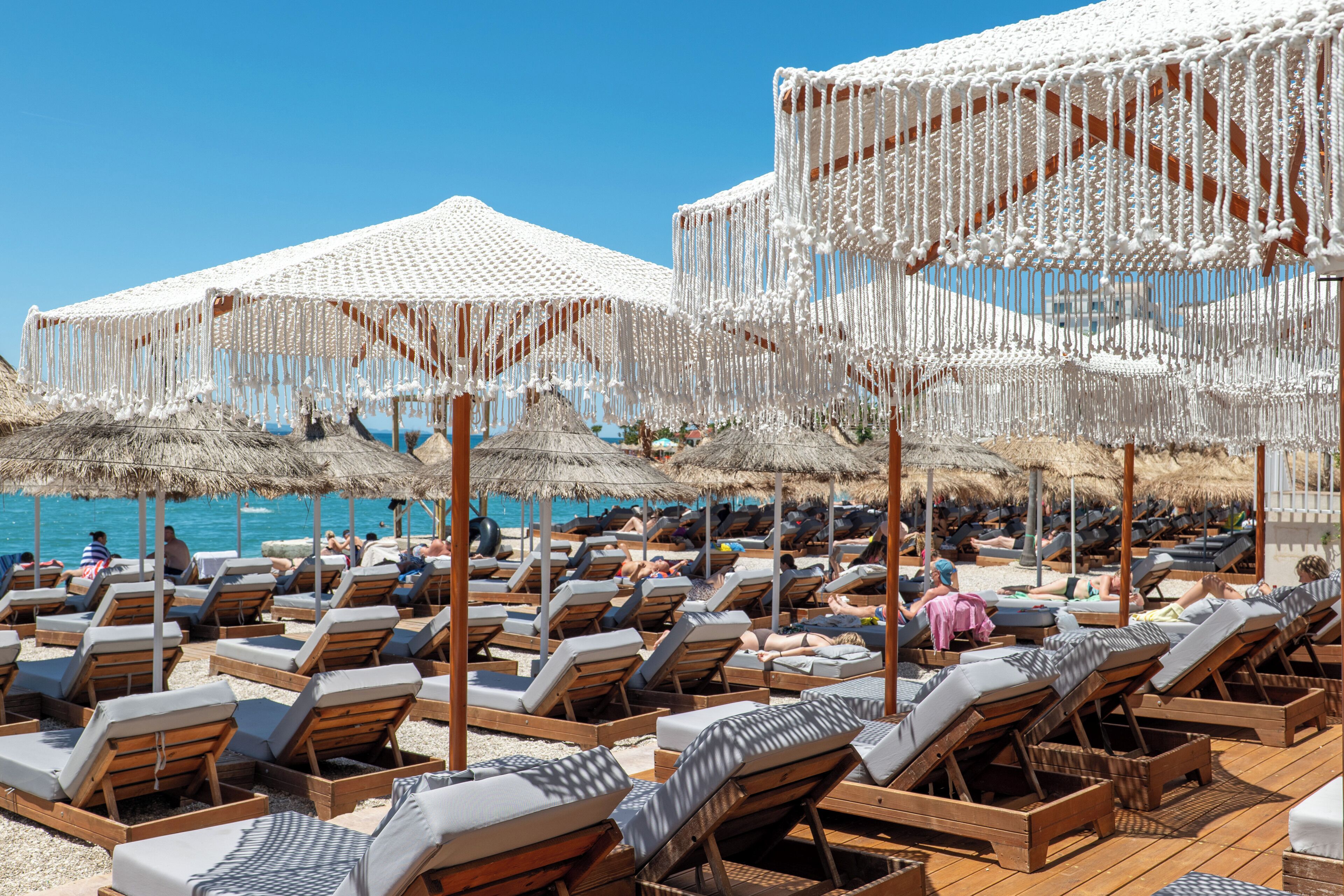 A beachside resort with rows of wooden lounge chairs and thatched umbrellas.