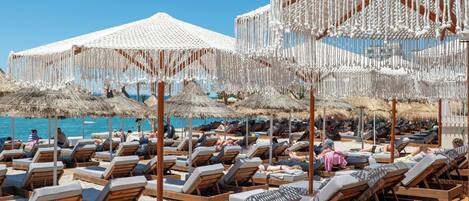 A beachside resort with rows of wooden lounge chairs and thatched umbrellas.