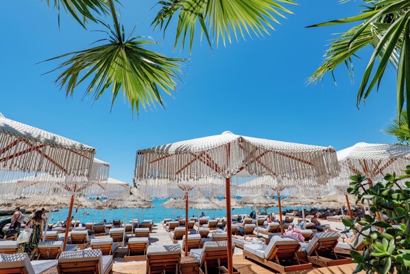 A beach with rows of sun loungers and thatched umbrellas.