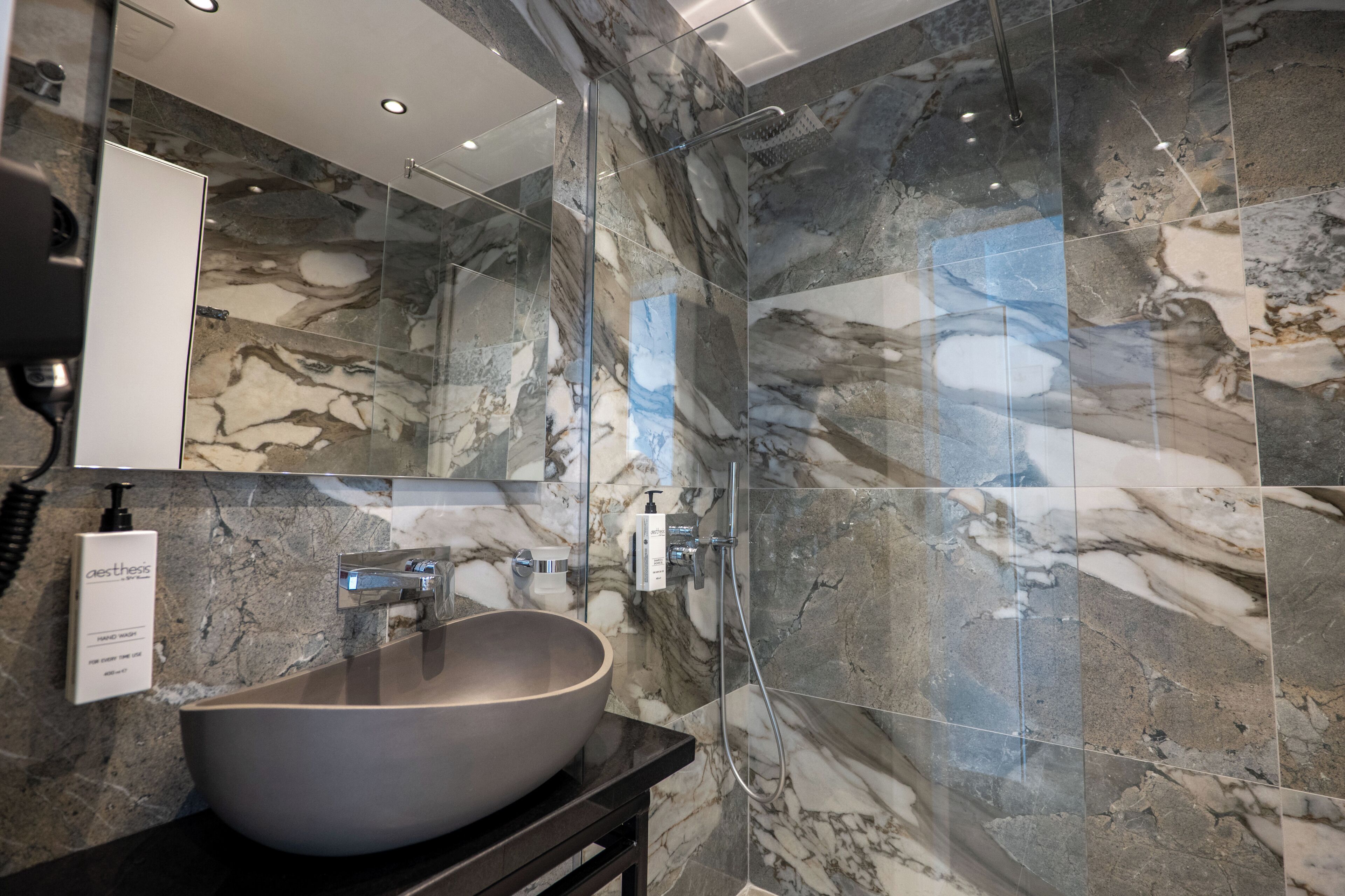 A bathroom with a large marble sink, a glass shower enclosure, and a mirror above the sink.