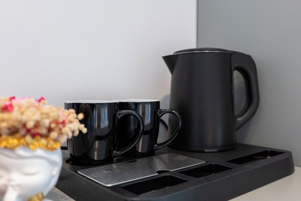 A coffee maker, two black mugs, and a flower arrangement on a countertop. - Vila Era Beach 2 (Sarande)