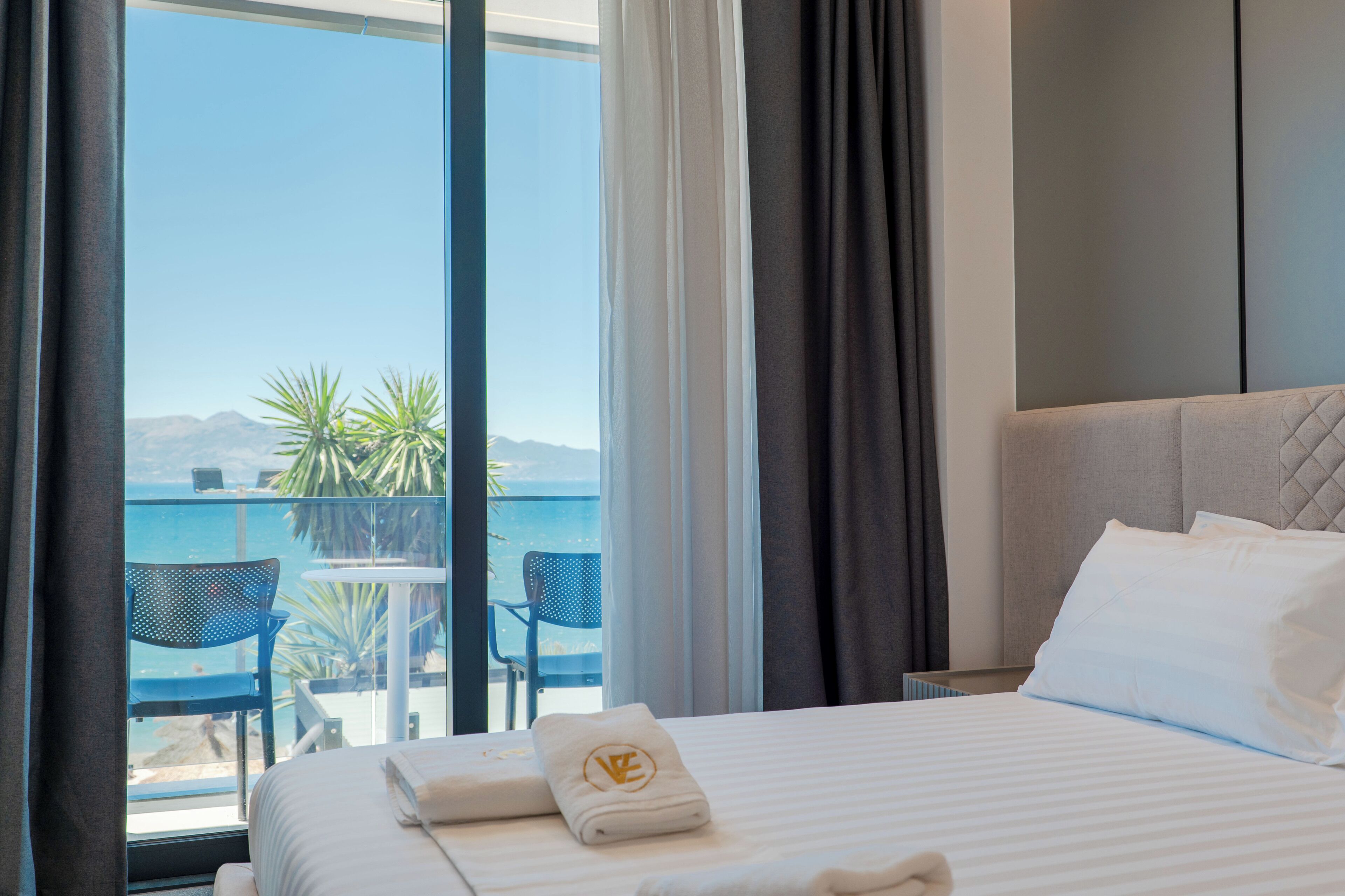 A hotel room with a bed, a view of the sea, a balcony with chairs, and a table.