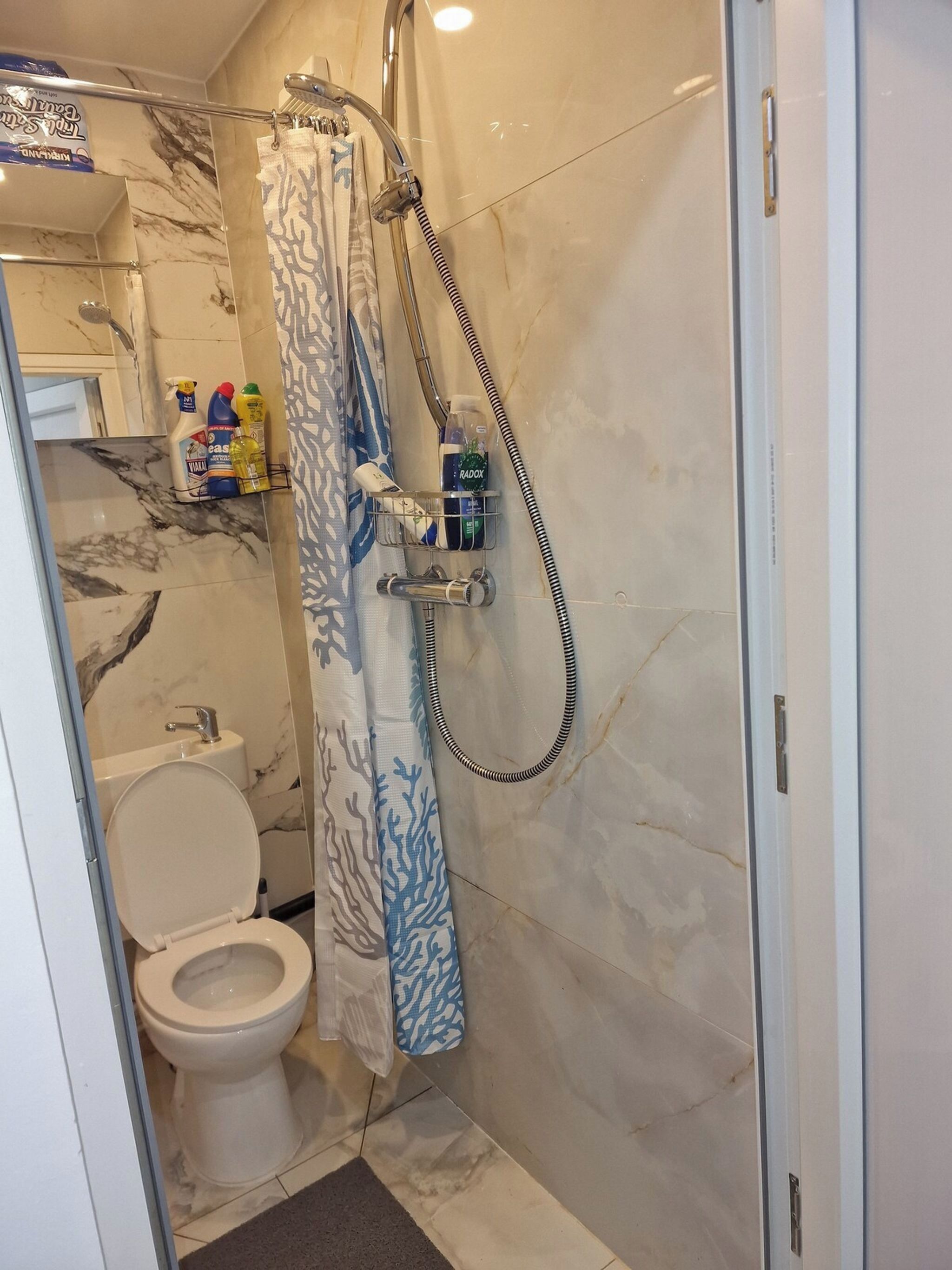 A bathroom with a toilet, shower, and marble walls.