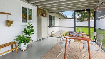 Une terrasse couverte avec une table et des chaises, des plantes en pot et une vue sur le jardin.