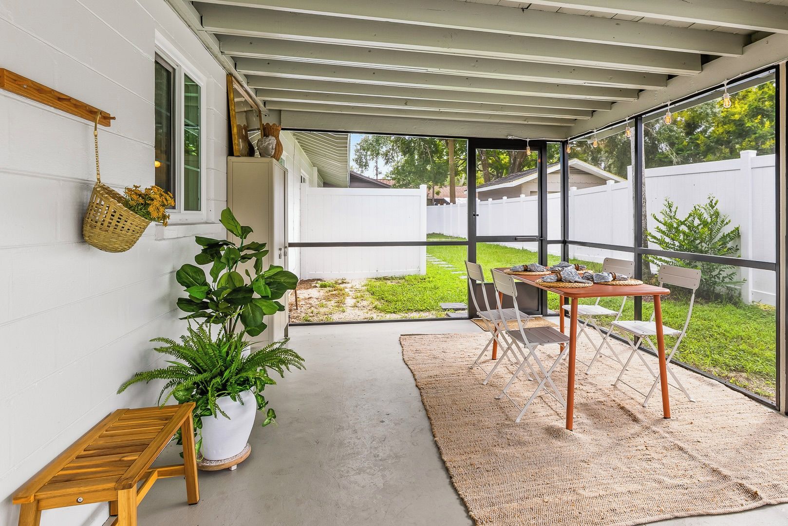A covered patio area with a table and chairs, a potted plant, and a hanging basket.
