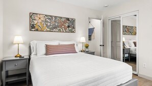 A neatly arranged bedroom with a bed, two bedside tables, a bench, and a door leading to another room. - Park the car and enjoy Mount Dora! <br>Stay just a 1/2 Mile from Downtown Mount Dora and Lake Dora in our beautifully restored 1950s duplex. <br>Walk to shops & dining! Features fast WiFi, workspace, patio, free parking, and boat parking! (Mount Dora)