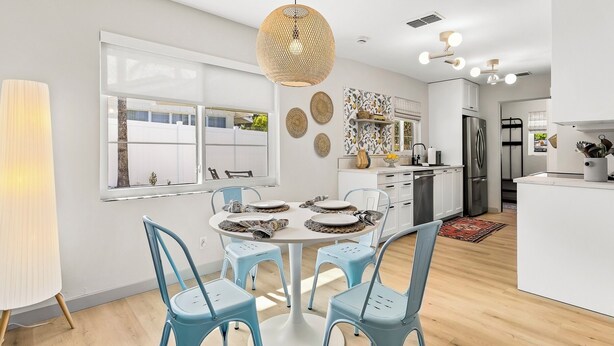 A modern kitchen with white cabinets, a stainless steel refrigerator, and a dining area with blue chairs and a round table. - Park the car and enjoy Mount Dora! <br>Stay just a 1/2 Mile from Downtown Mount Dora and Lake Dora in our beautifully restored 1950s duplex. <br>Walk to shops & dining! Features fast WiFi, workspace, patio, free parking, and boat parking! (Mount Dora)