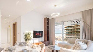 Una sala de estar moderna con comedor, televisor montado en la pared y vista a un edificio de gran altura.