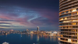 Un hotel de gran altura con varios balcones, vista al agua y el horizonte de la ciudad al fondo.