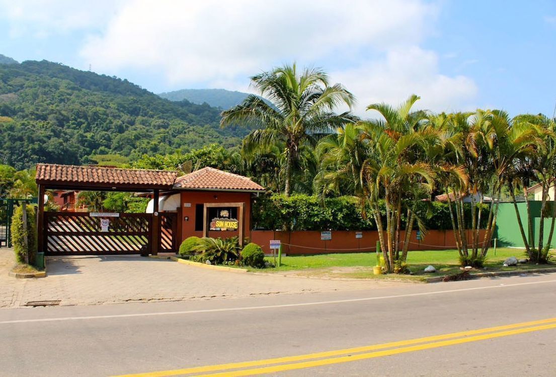 Entrada de hotel con un camino de acceso vallado, palmeras y montañas al fondo.