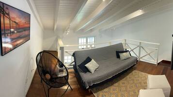Una habitación estilo loft con techo alto, un sofá a rayas, una silla negra y un cuadro de un muelle.