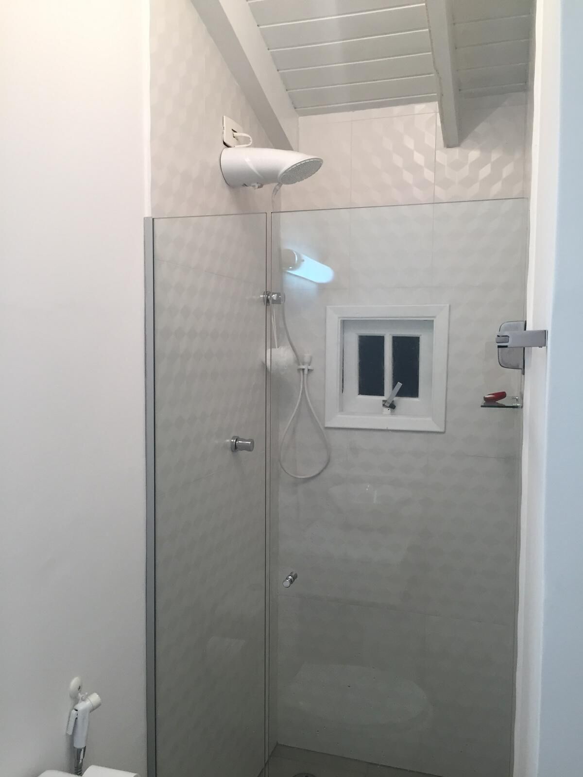 Une douche fermée par des parois en verre, dotée d’un pommeau de douche à main, d’une petite fenêtre et d’un porte-serviettes.
