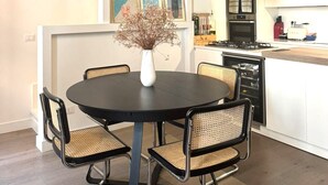A modern kitchen with a dining area, featuring a round table, four chairs, a vase with dried flowers, and a black pendant light. - Colosseum Luxury Retreat (Roma)
