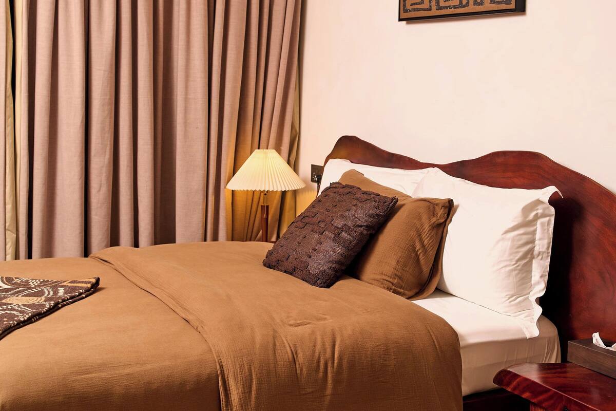 Ein Hotelzimmer mit Bett, Vorhängen, einer Lampe und einem Wandbild.