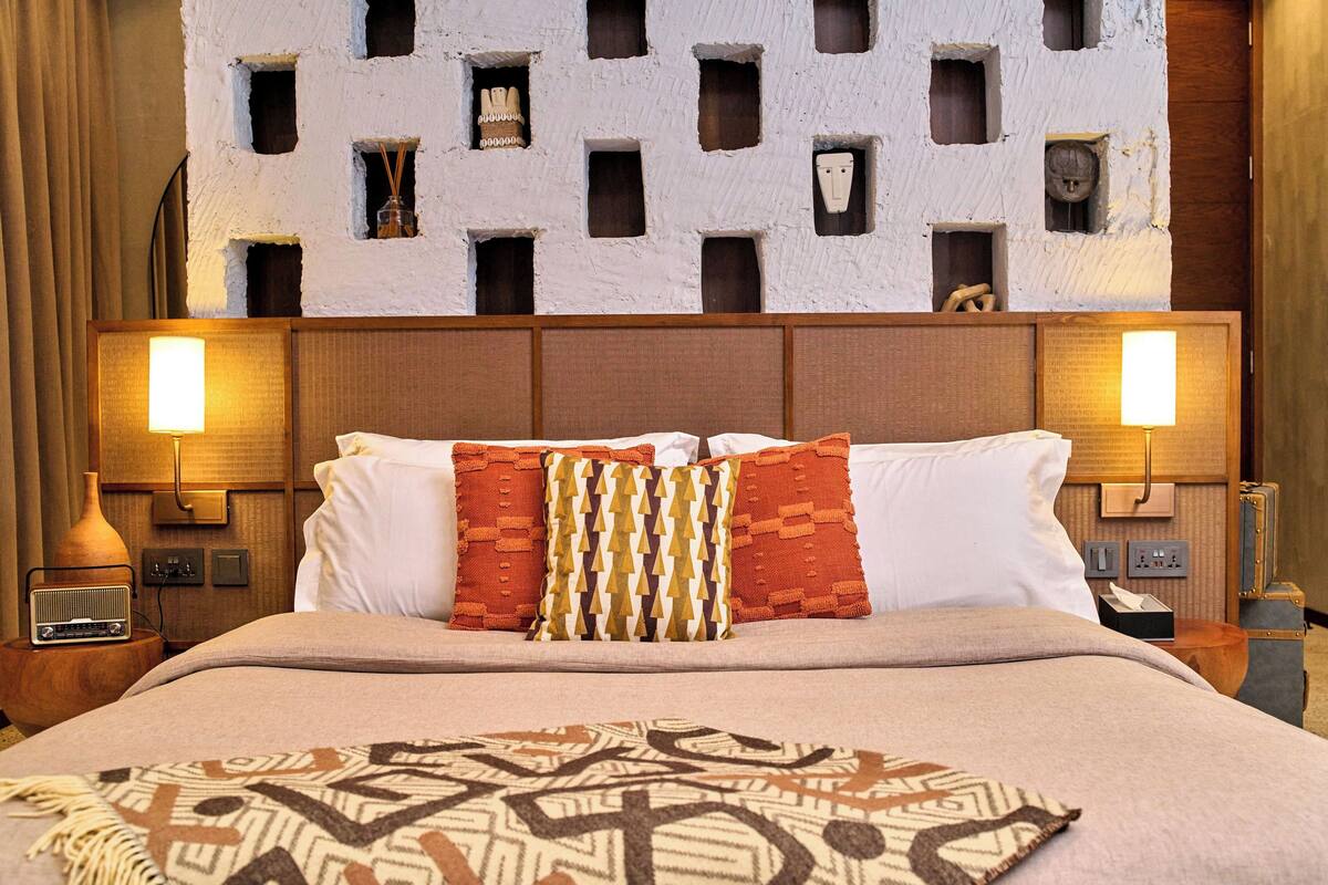 Ein Hotelzimmer mit einem großen Bett, zwei Nachttischlampen, einer gemusterten Tagesdecke und einer Wand mit quadratischen Aussparungen.