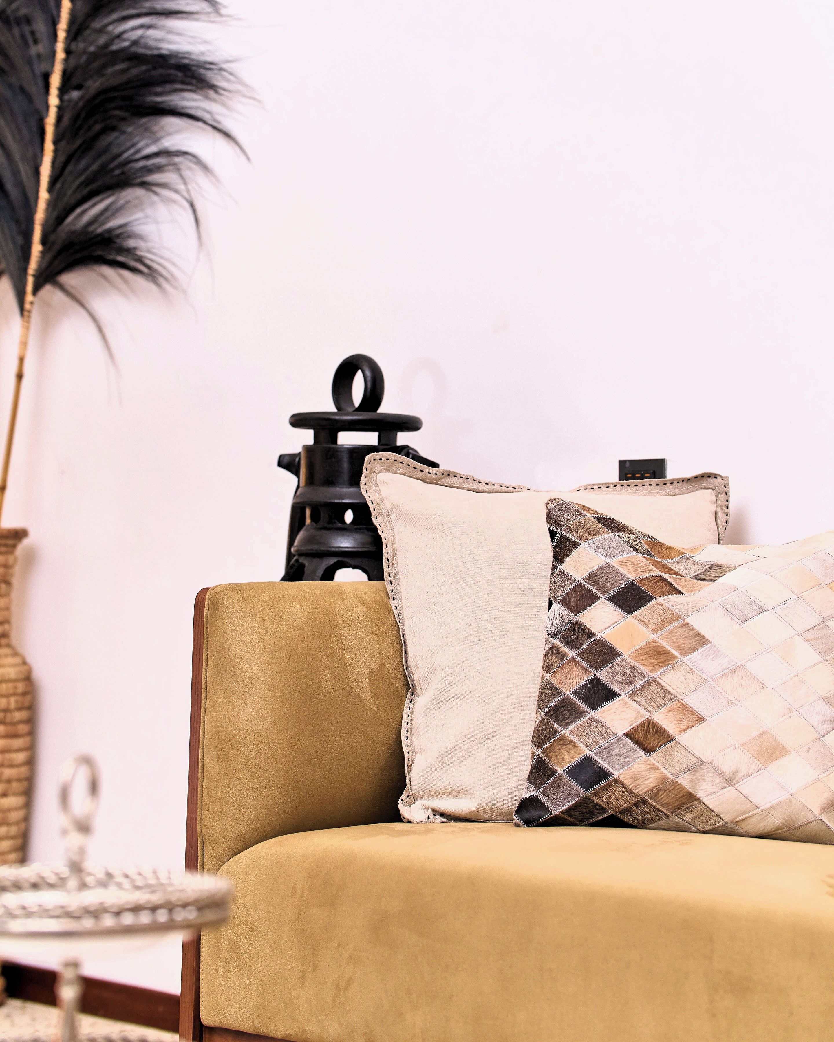 A sofa with two pillows, a lamp, and a vase with a plant.